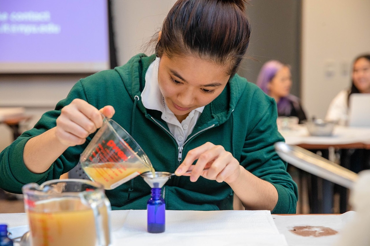 Student pouring herbal concoction into bottle