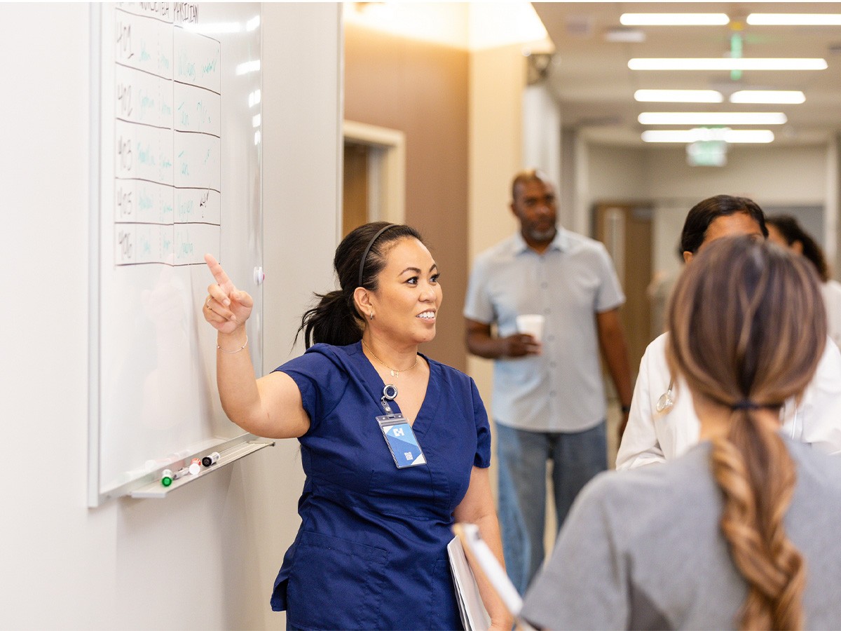 Hospital Nurse Manager talking to nurses and  pointing to something on the wall calendar