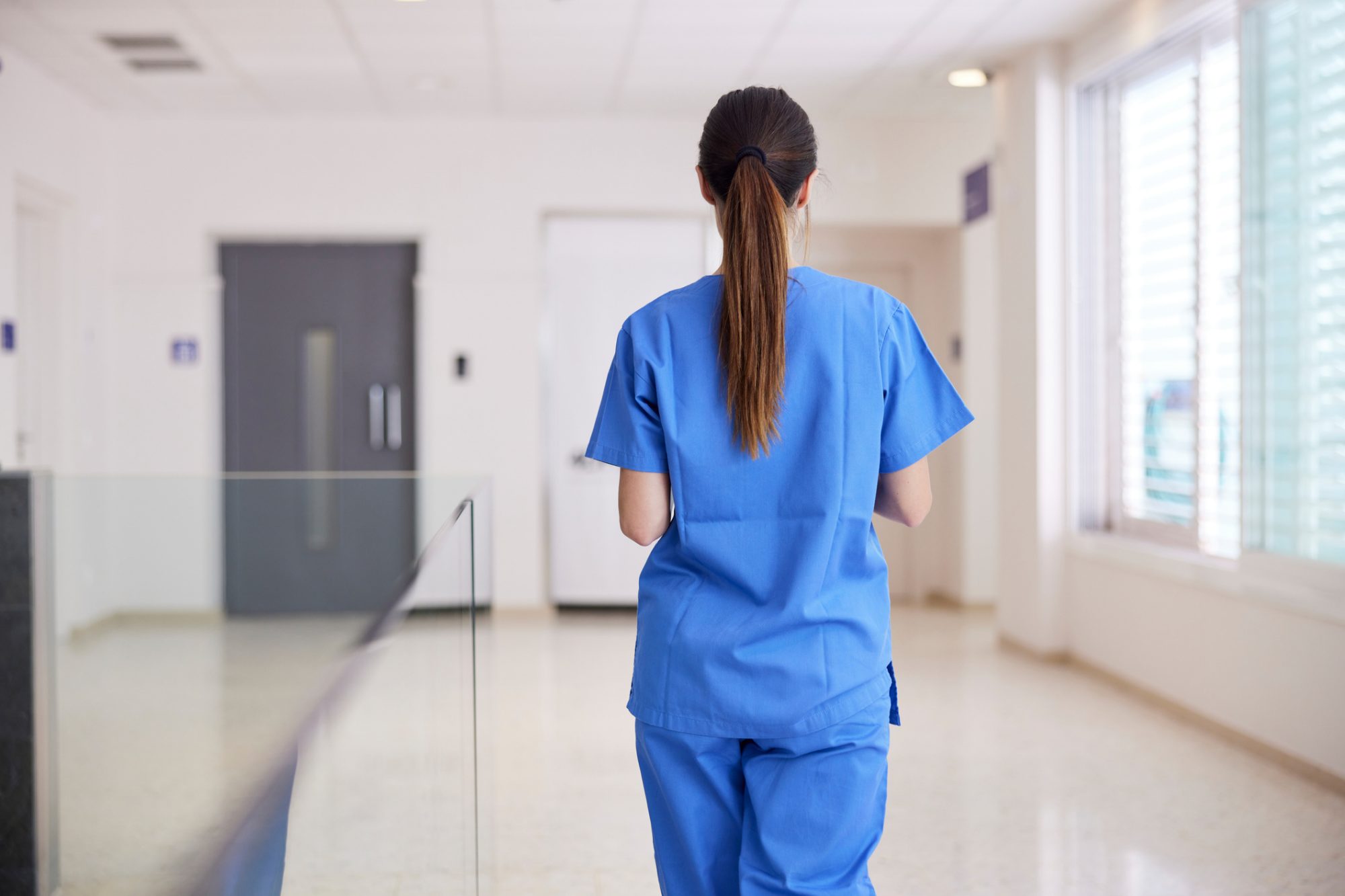 Back of a women nurse in blue scrubs walking down a hallway