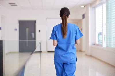 Back of a women nurse in blue scrubs walking down a hallway