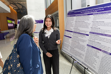 young women presenting research poster to faculty