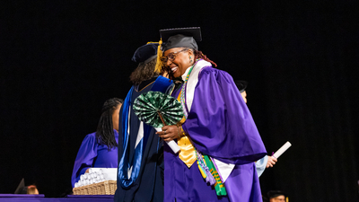 Jasmin LeCadre hugging professor on stage at graduation ceremony