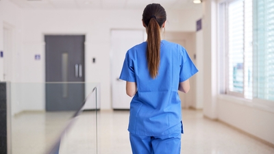Back of a women nurse in blue scrubs walking down a hallway